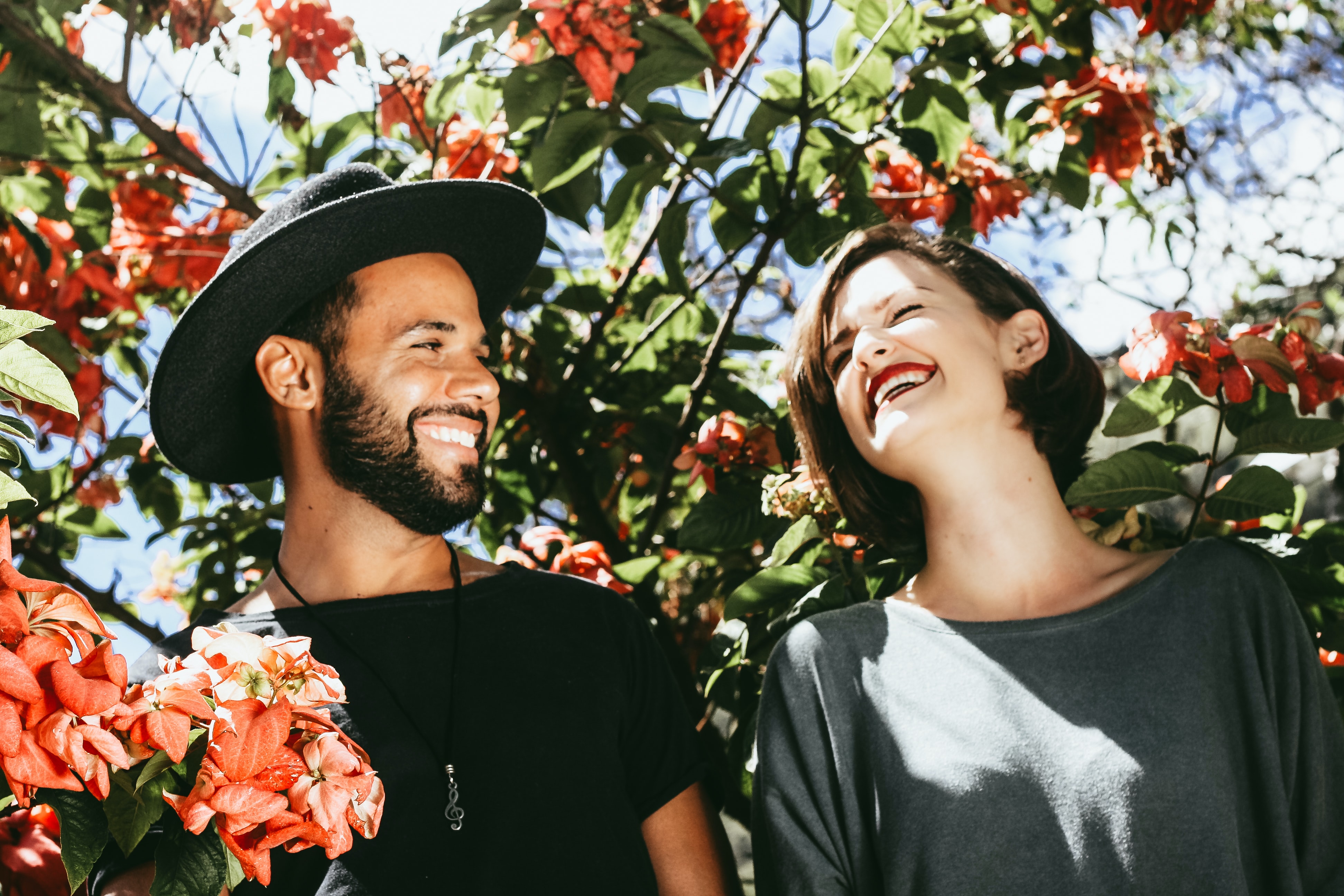 Image of an attractive man and woman with stylish clothes laughing looking at each other surrounded by red flowers.