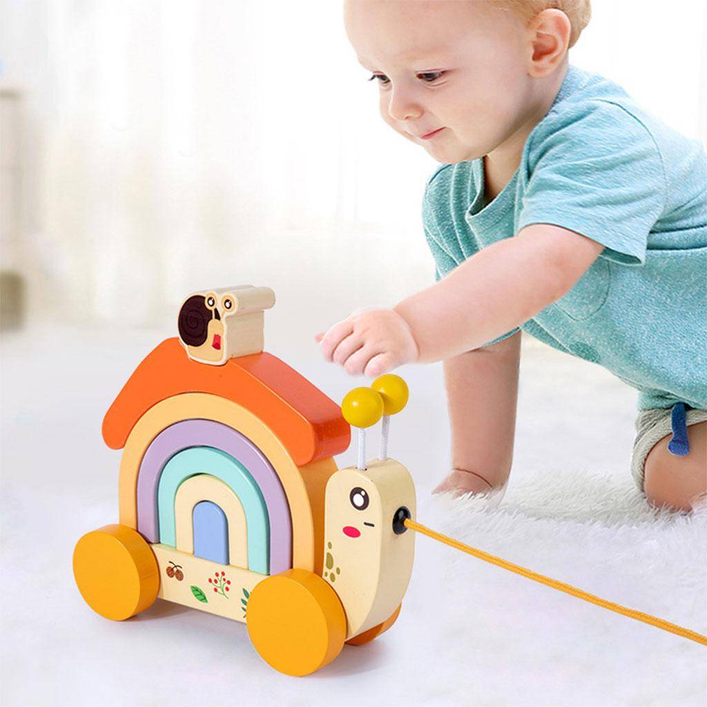 Un tout-petit joue attentivement avec un escargot à tirer Montessori InvenToy coloré et écologique sur roues, sur un fond blanc doux.