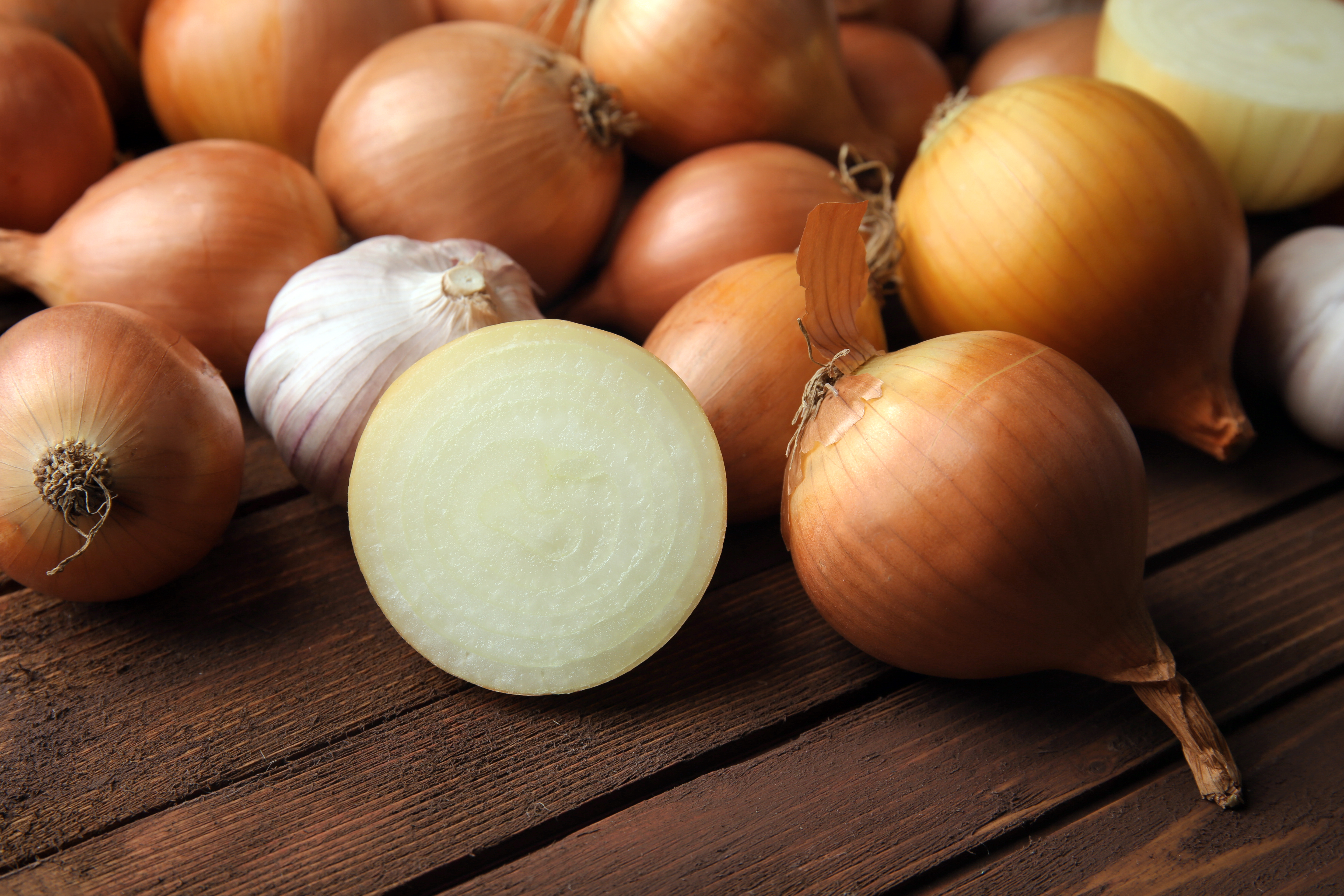 Several whole yellow onions with one cut onion and a garlic bulb on a wooden background