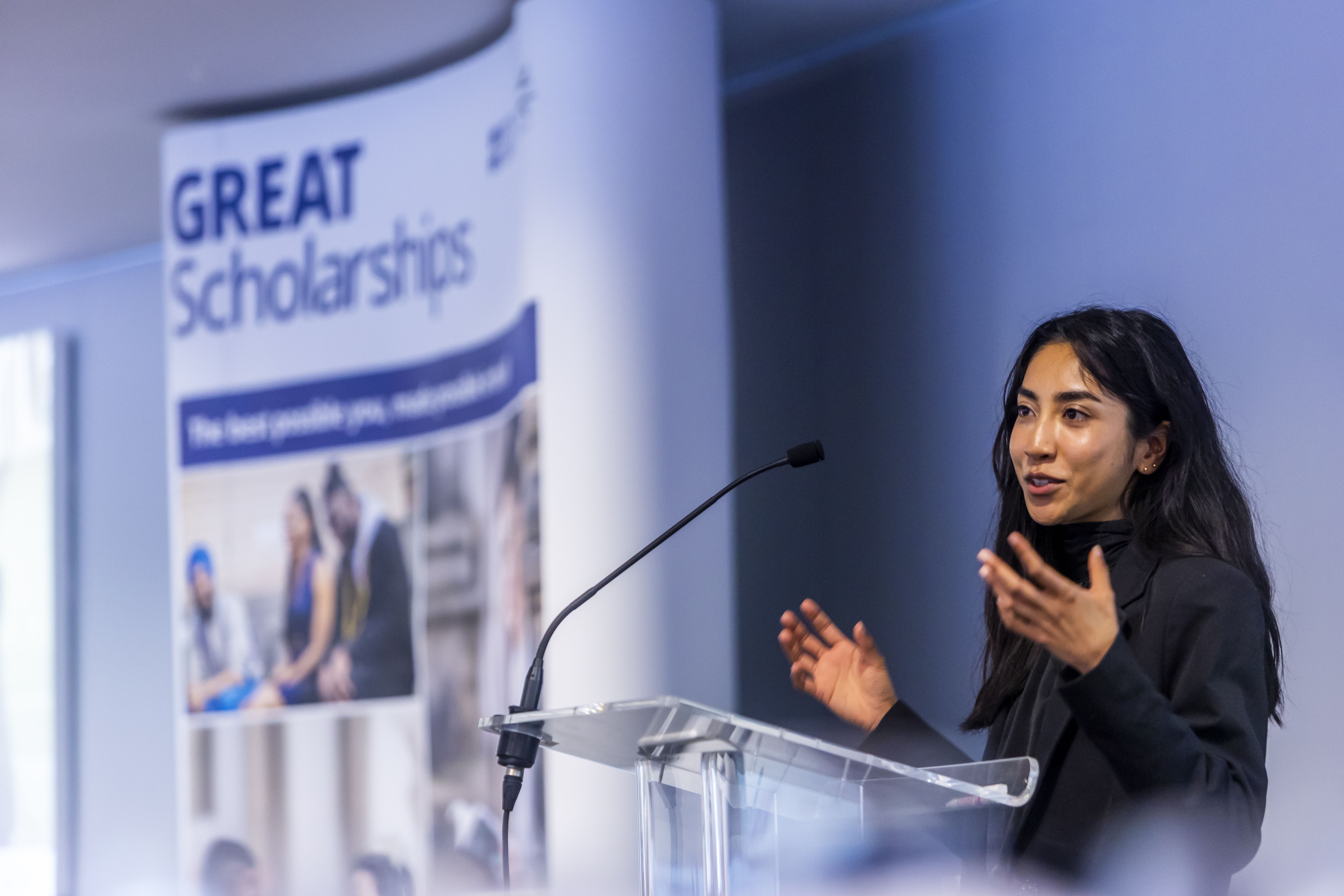 GREAT scholar Chrislyn Pereira from Malaysia stands behind a podium gesticulating passionately to the audience. She is beside a banner that says 'GREAT Scholarships'