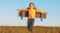 Child pilot aviator with wings of airplane dreams of traveling in summer at sunset