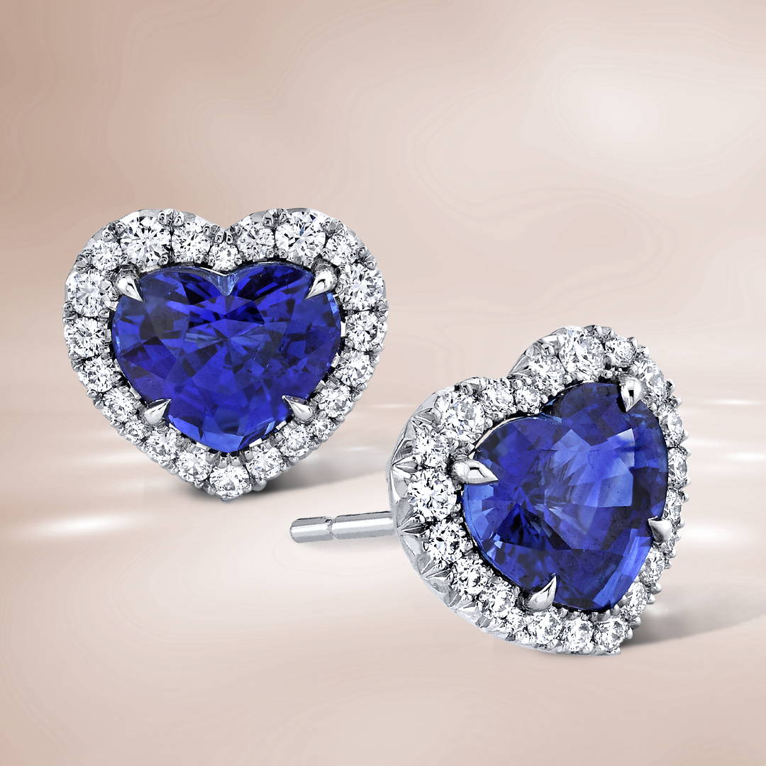 Heart shaped sapphire stud earrings with diamond halo on a brown background