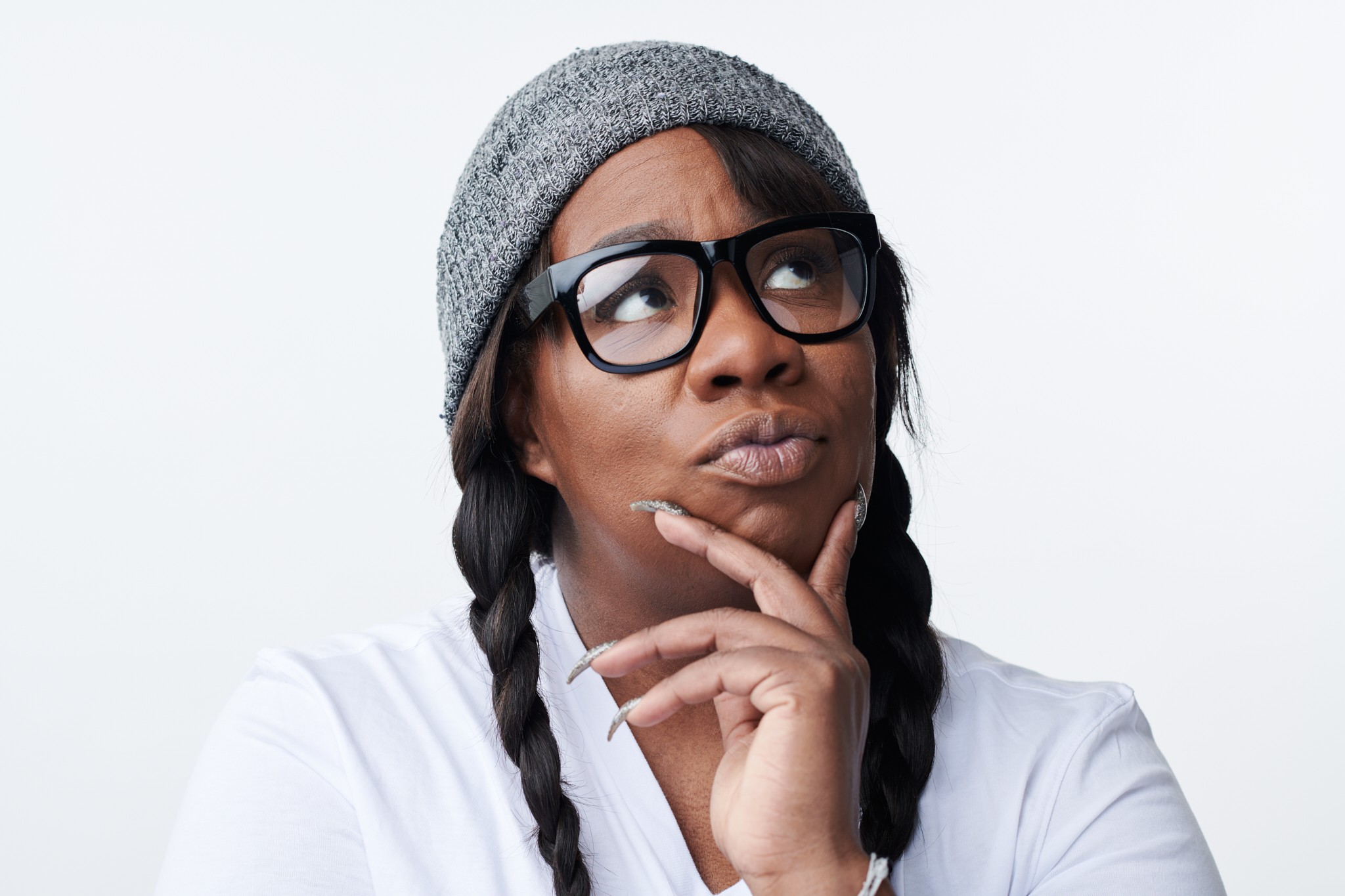 Franqi French holding her hand up to her chin looking pensive towards the cieling. She is wearing her hair in braids with a beanie and glasses.