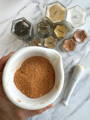 An orangeish brown ground spice in a white bowl surrounded by glass spice jars