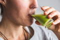 close-up of a woman drinking a green wheat grass shot