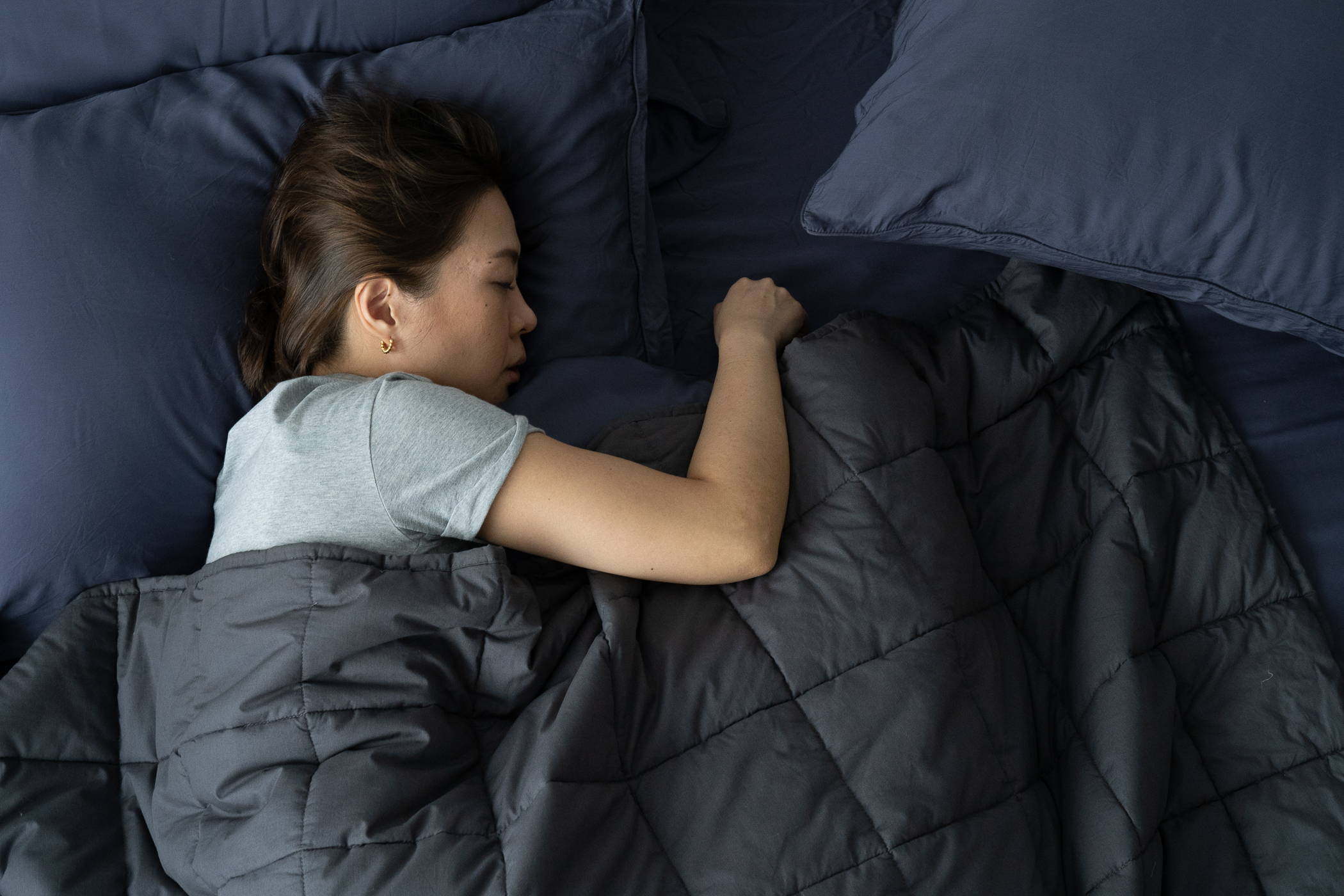 Midshot of woman sleeping on bed with pillows and weighted blanket