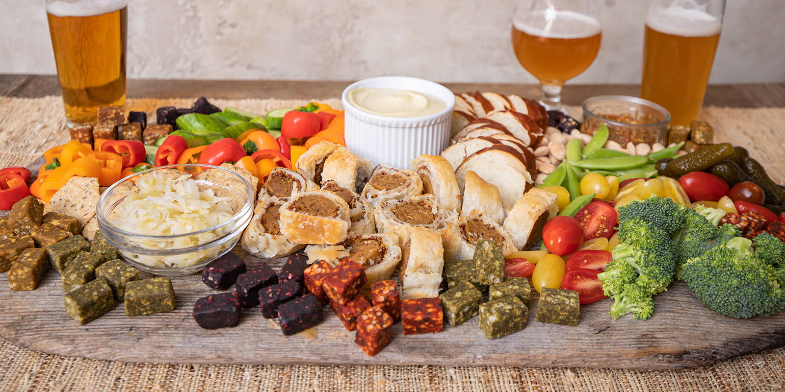 Vegan grazing board with vegetables, vegan cheese, and plant-based meat, paired with beers.