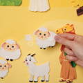 Woman's hand holding felt sheep cutouts featured in the Montessori Nativity Wallboard set.
