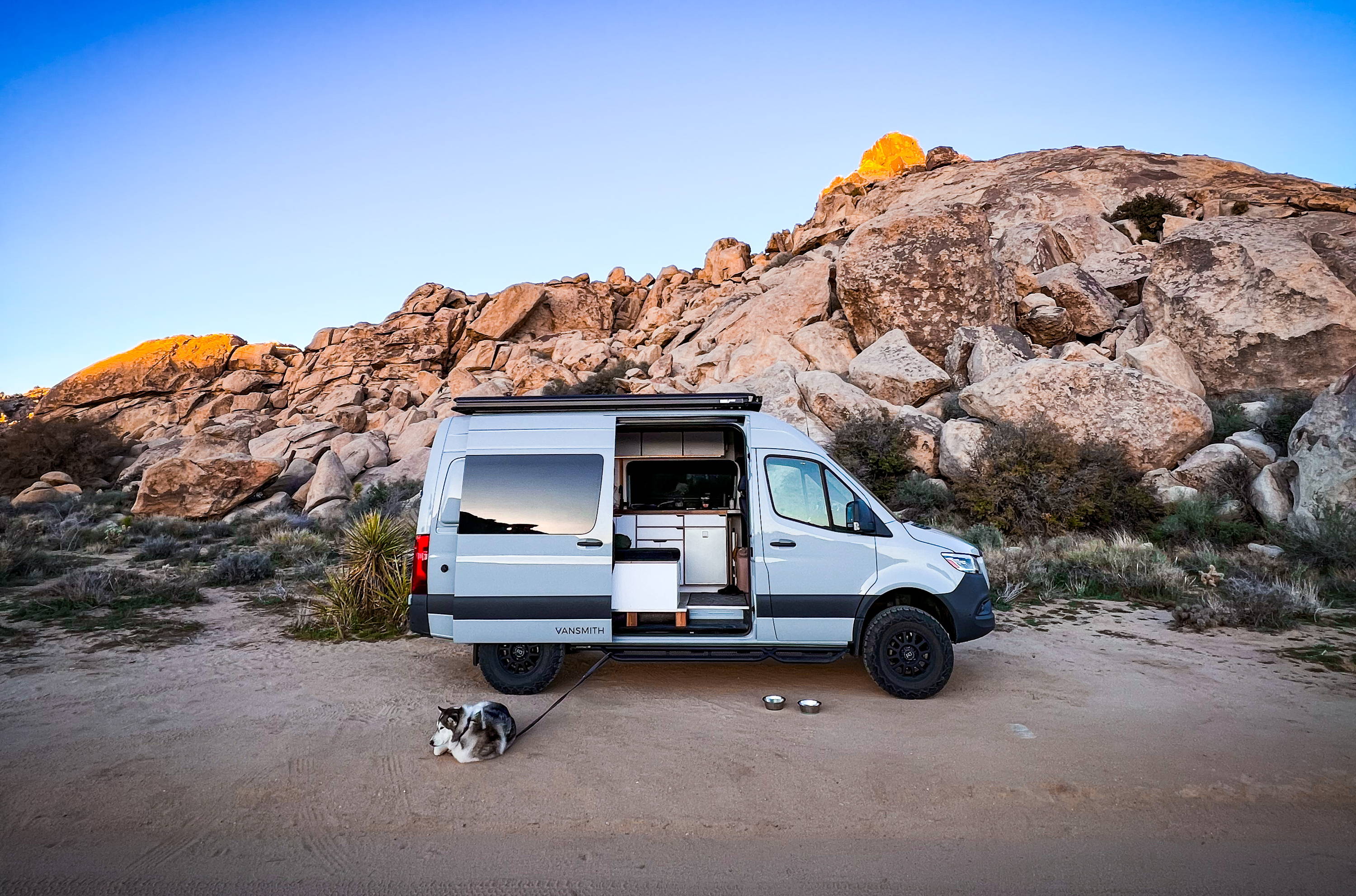 Sprinter Van Conversion Built by The Vansmith in Front of Desert Rocks with Husky Resting Outside