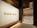 Hotellobby mit beleuchteter Treppe, Holzlatten-Decke, Holzbank und goldener 'ROW NYC'-Beschriftung.