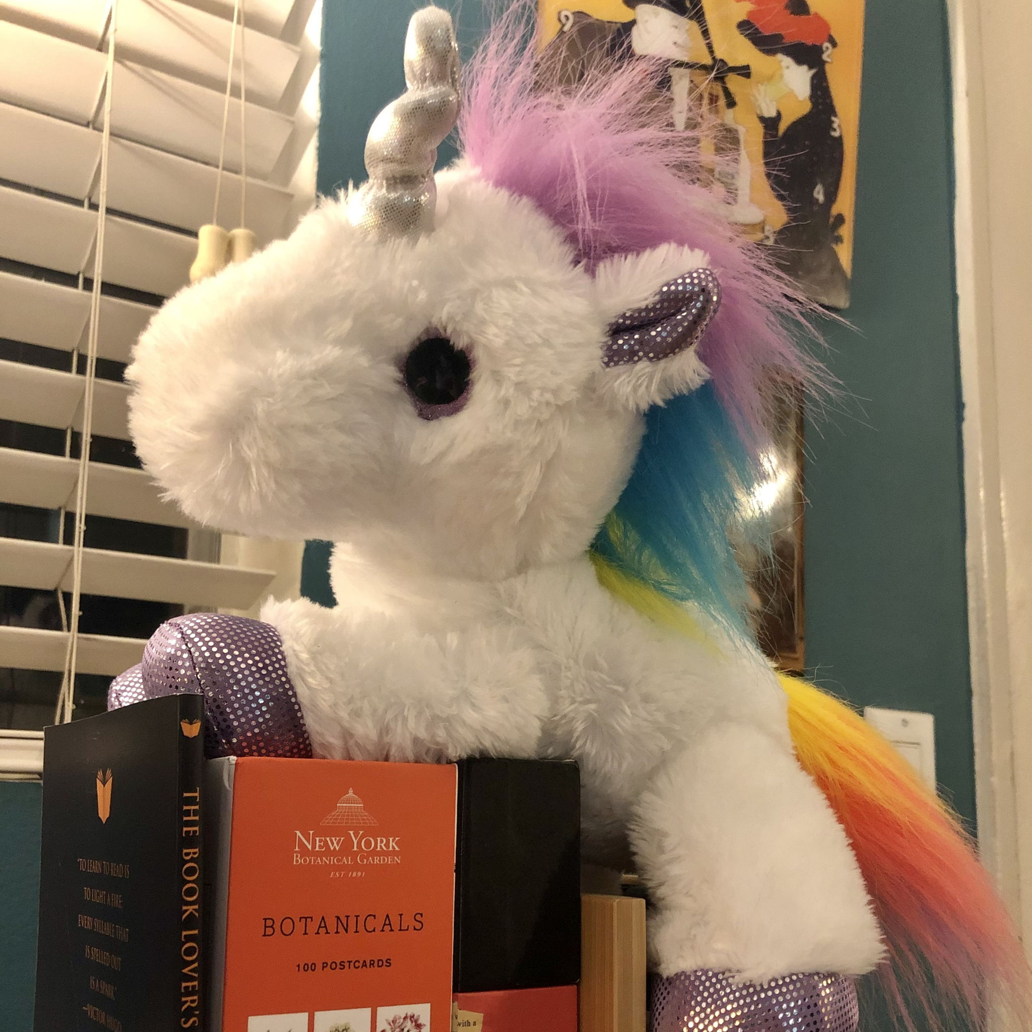 A plush Unicorn sitting on a pile of books.