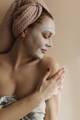 Woman with a towel on her hair doing a face treatment for dewy skin