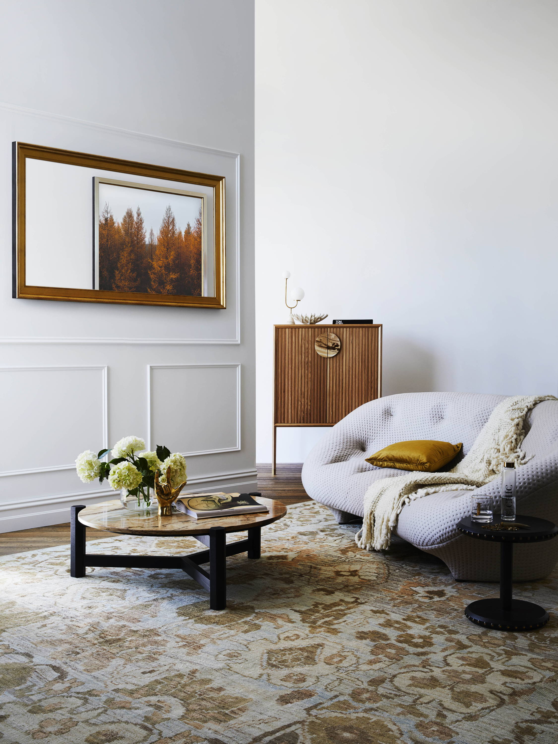 A living room setting with a TV Mirror in a gold frame on the wall.