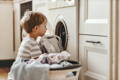 Little boy putting dirty clothes in the washing machine. 