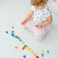Little girl sitting on the floor and playing with wooden alphabet letters.