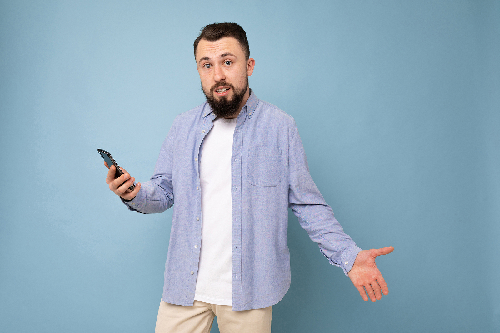 Surprised young man with a phone in his hands against a background of a blue wall