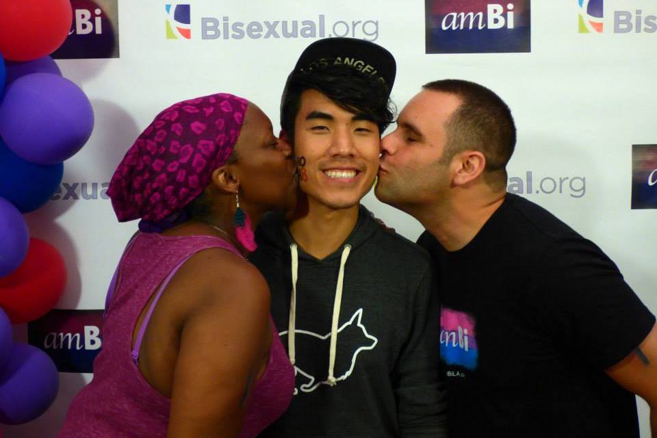 A man and a woman kiss an Asian man in the cheek while he smiles at a ambi event.
