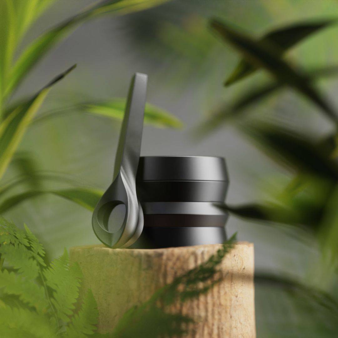 Black KLIP grinder and KOL pipe over wood and surrounded by green plants