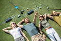 Four friends lying on grass enjoying music with wireless paired portable golf speakers.
