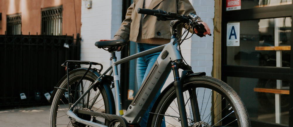 a woman standing next to a silver Gazelle Ultimate C380+ electric commuter bike