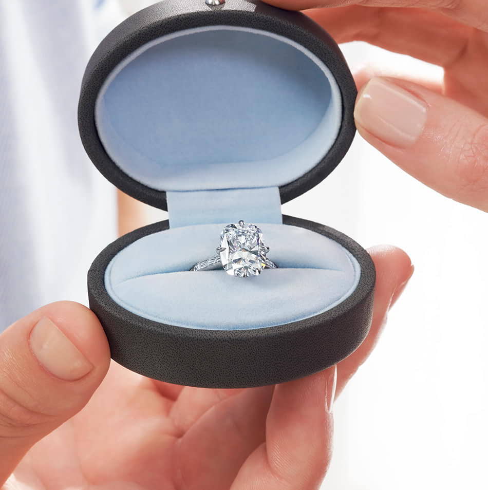 Person opening a ring box holding a Kwiat Cushion Diamond ring .