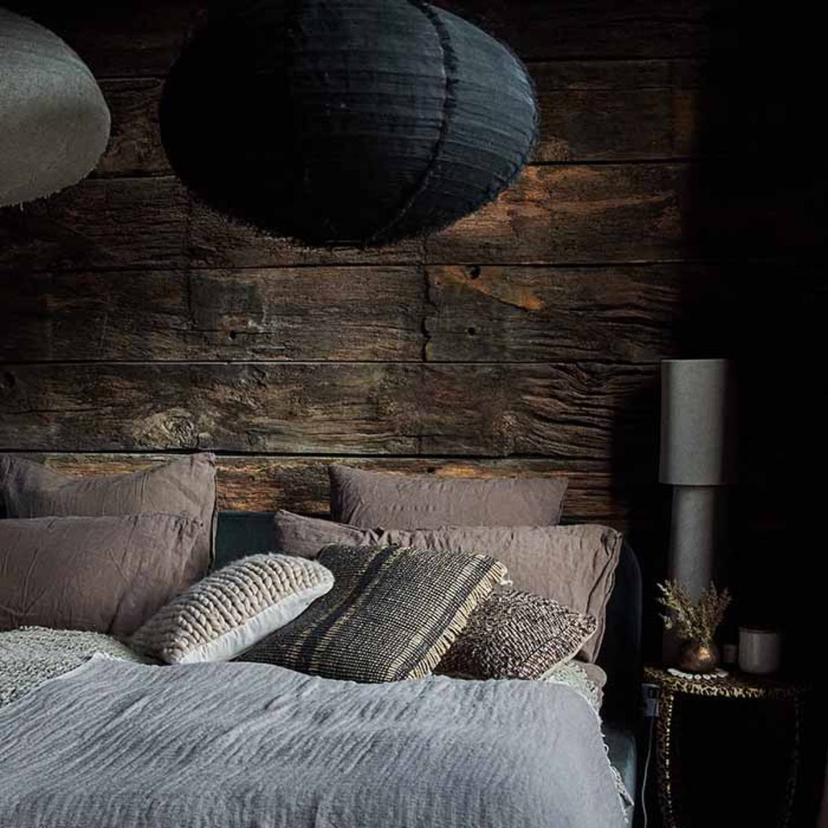 A bed made with lots of cushions and a linen throw set against a background of a wall made with reclaimed wood 