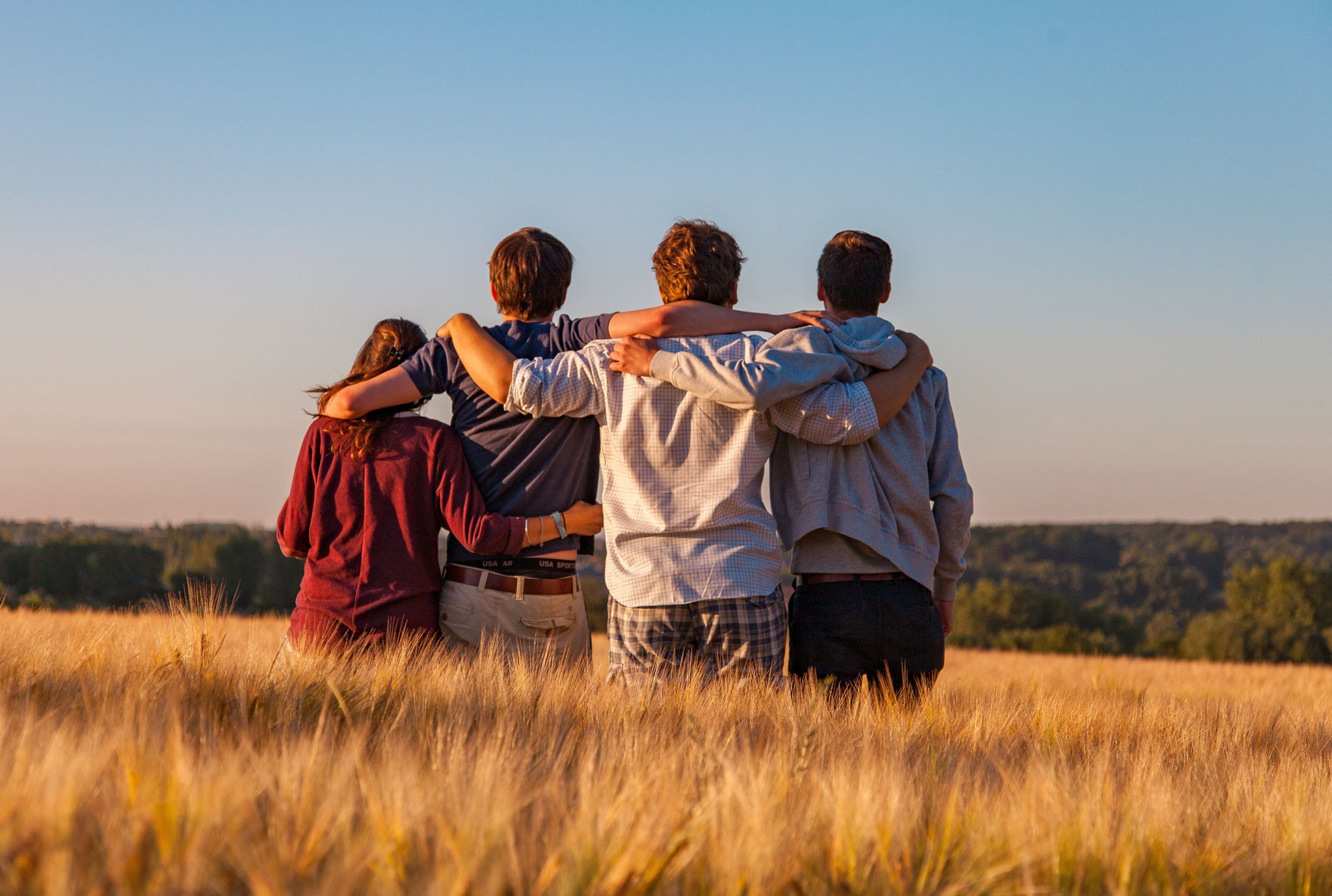 A group of friends hugging each other looking at a sunset.