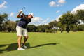 Male golfer executing a powerful full backswing with a iron on a sunny fairway.