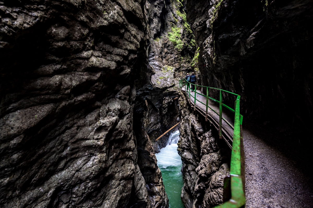 The sun peeks into the Breitach Gorge; a bridge spans the gorge; the water is clearly visible