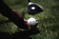 Golfer placing a TaylorMade golf ball on a tee with driver in background.