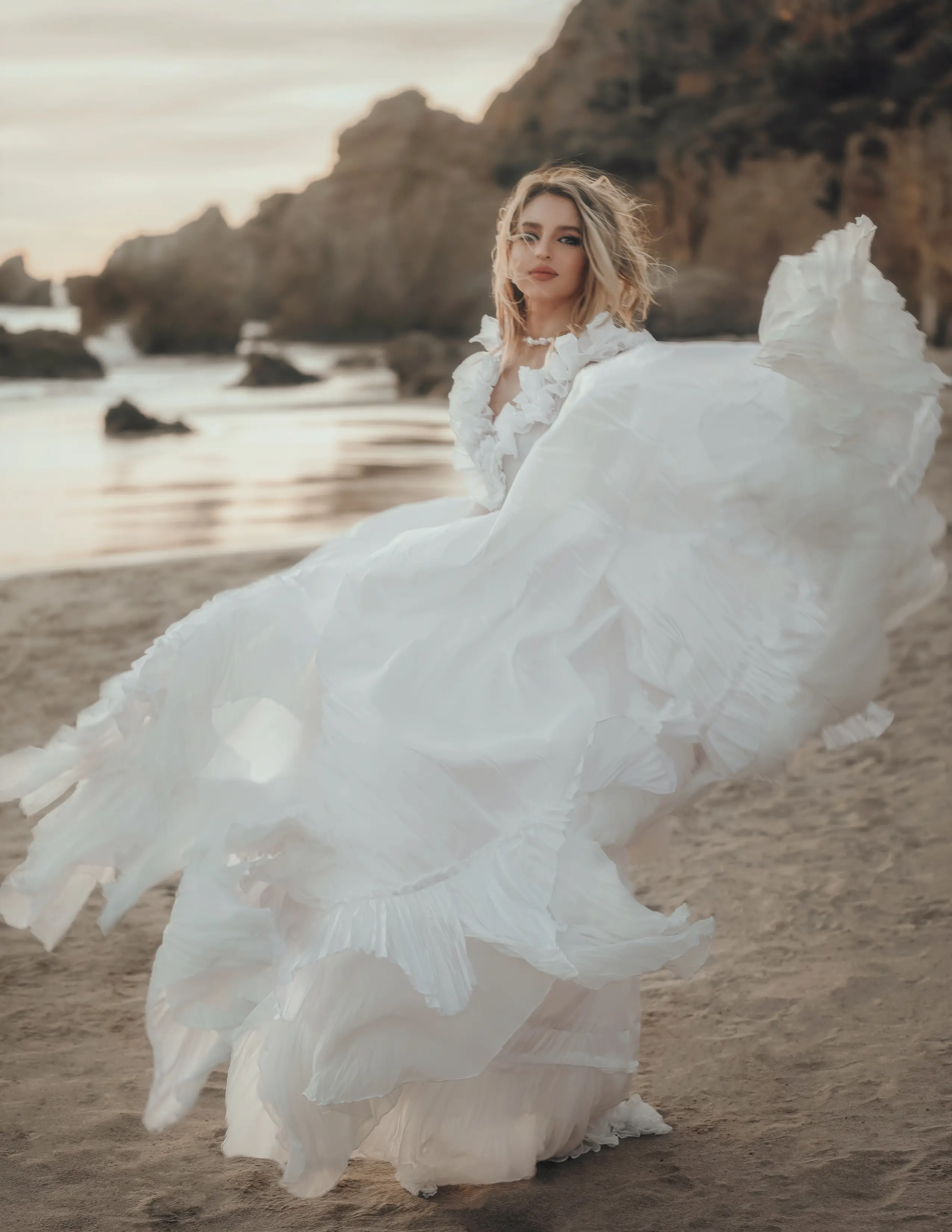 Une mariée se tenant sur la plage, portant une robe de mariée blanche, avec les vagues de l'océan en arrière-plan.