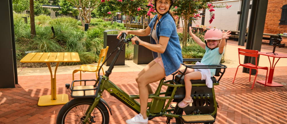 a woman riding a denago electric cargo bike with her child on the back