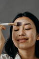 Woman using a face brush to put on a dewy skin treatment