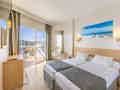 Helles Hotelzimmer mit zwei Einzelbetten, Schreibtisch, strandthematischer Kunst und einem Balkon mit Stadtblick.