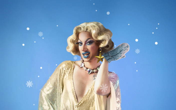 A Drag Queen wearing mittens surrounded by snow for Confetti's Virtual Bingo Game