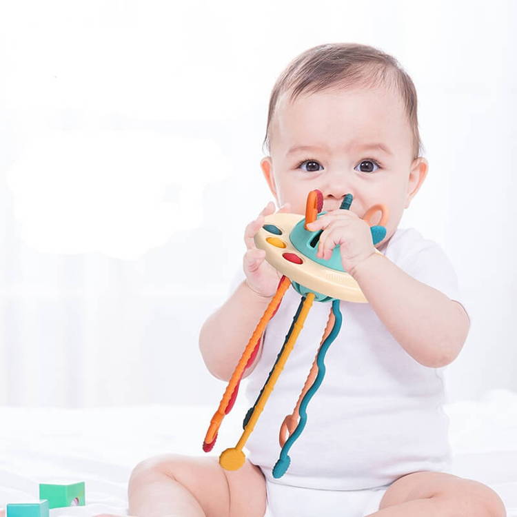 A baby holding and chewing a Montessori pulling toy made out of silicone.